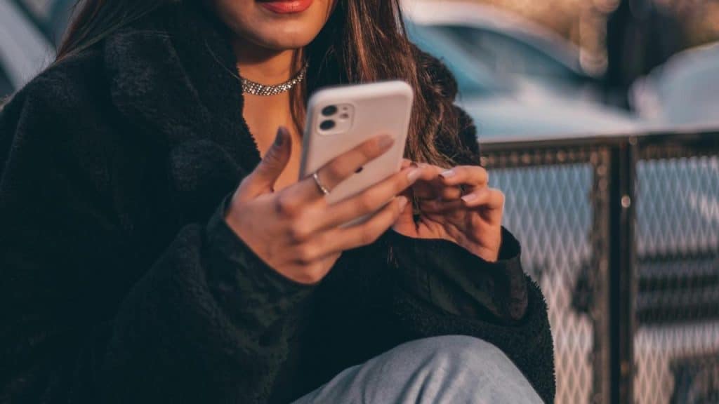 A woman holding and using a smartphone while sitting outdoors.
