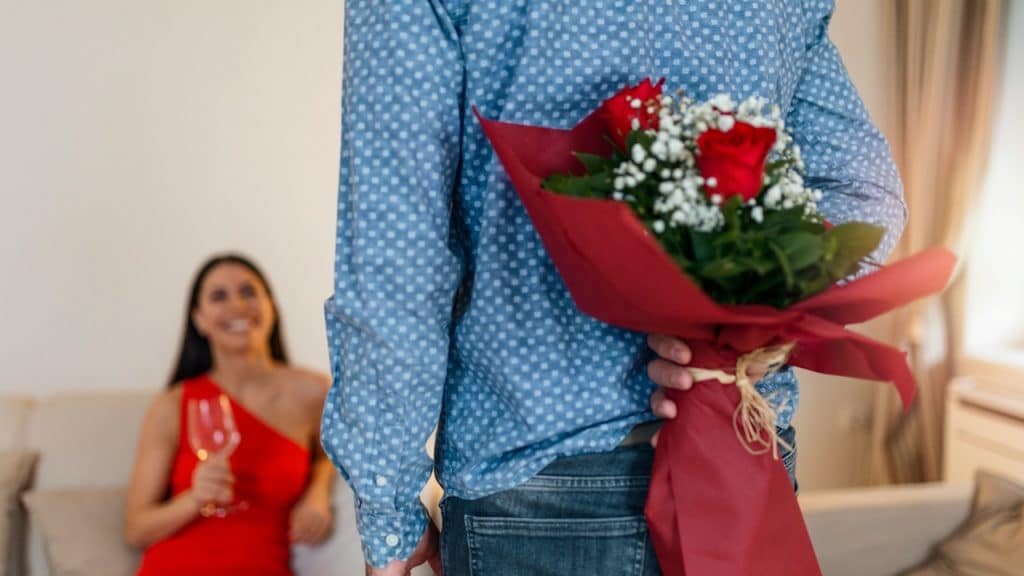 A handsome man holding flowers behind his back to surprise his girlfriend.