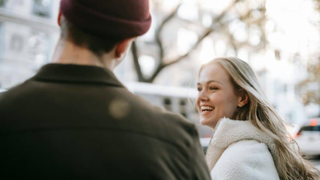A smiling blonde woman looks at a man who is shown from behind.