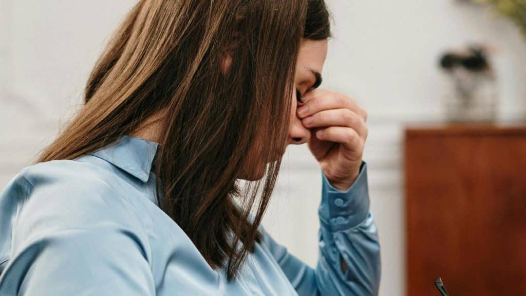 A stressed woman sitting with her hand on her forehead.