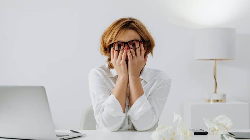 A stressed woman covering her face while sitting at a desk.