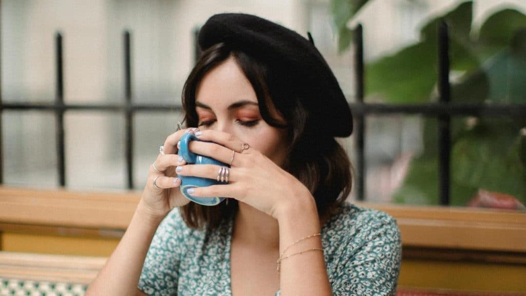 A woman drinking from a cup while outside a restaurant.