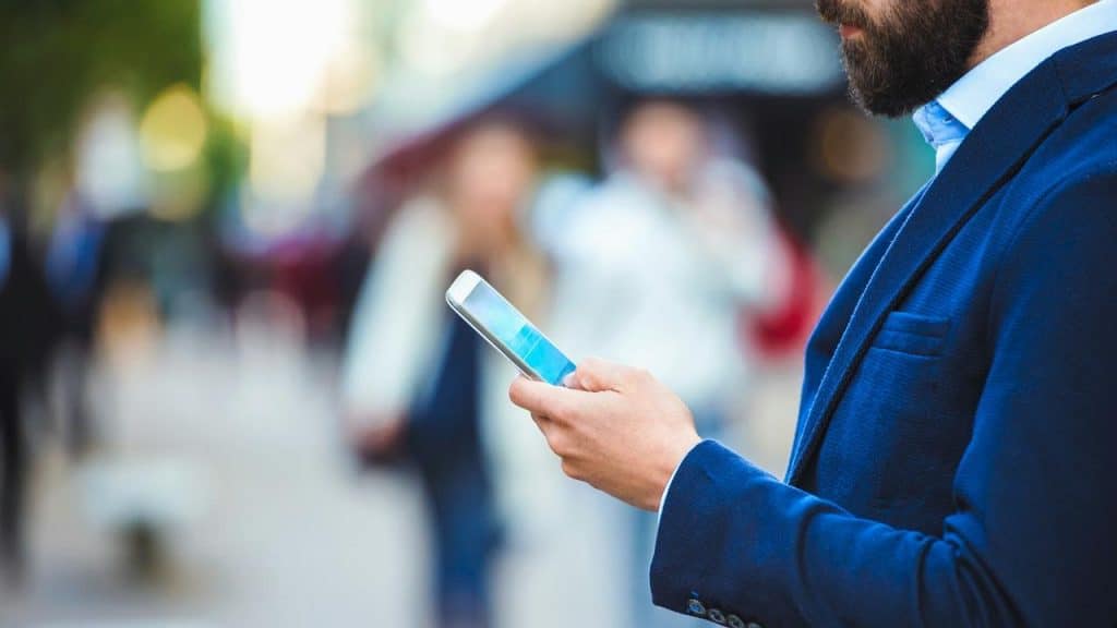 A man in a blue suit using a smartphone outdoors.