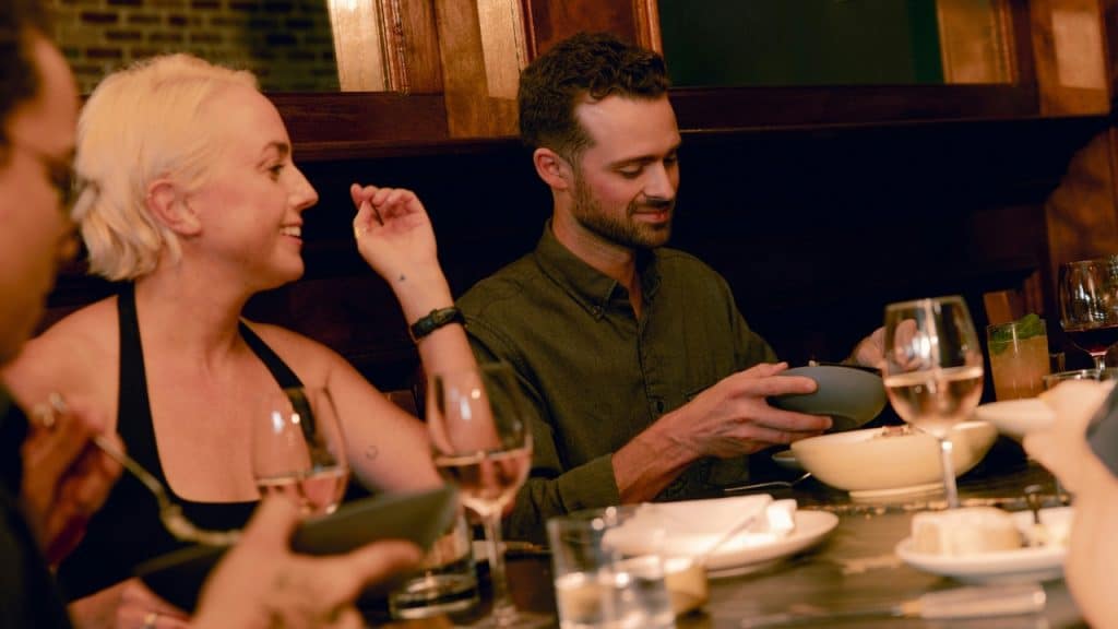 A woman with blonde hair smiles and talks to a man eating at dinner.