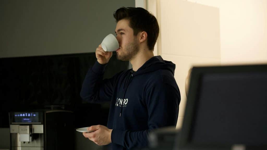 A man drinking coffee in a kitchen while holding a cup and saucer