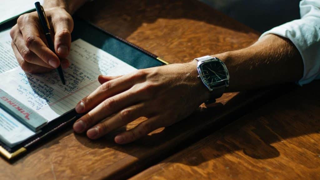 A person writing notes on paper at a wooden desk.