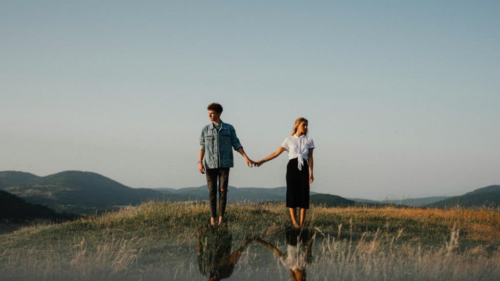 A young couple standing in nature holding hands but looking away
