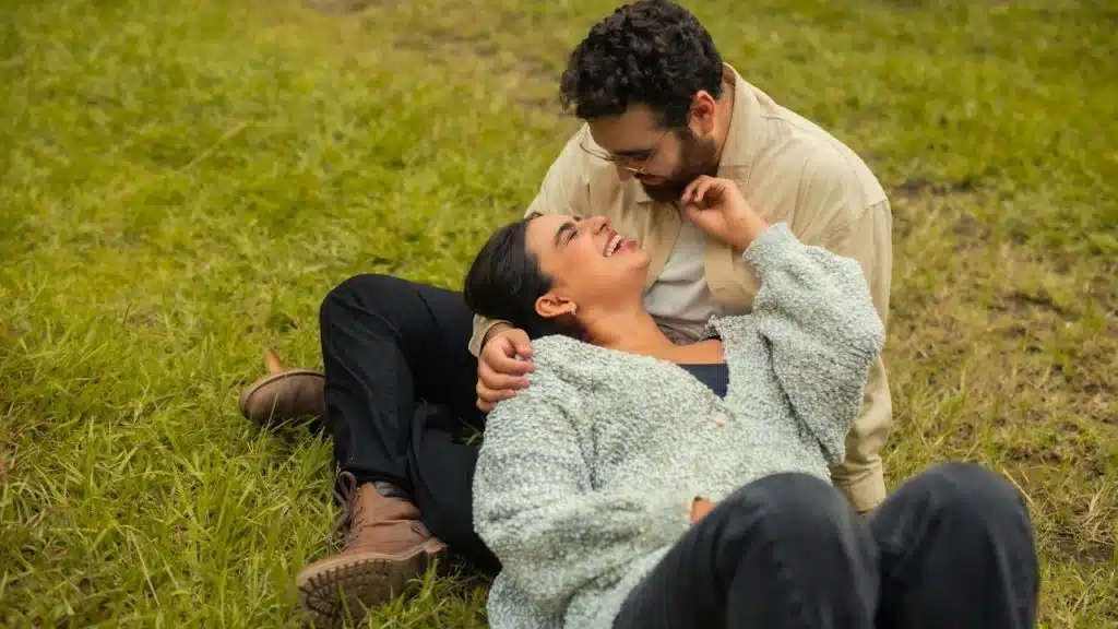 A laughing woman rests her head in a bearded man’s lap, and he looks at her face and smiles.