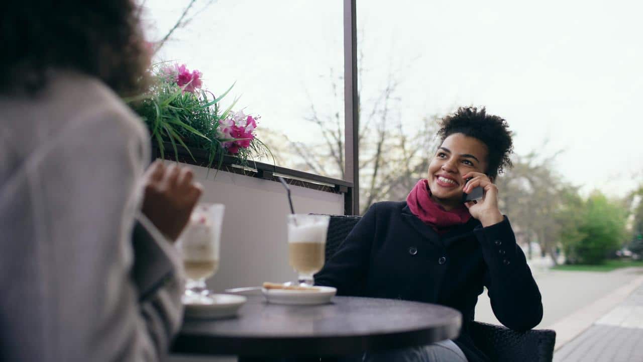 A woman smiling while talking on her phone at an outdoor café table.