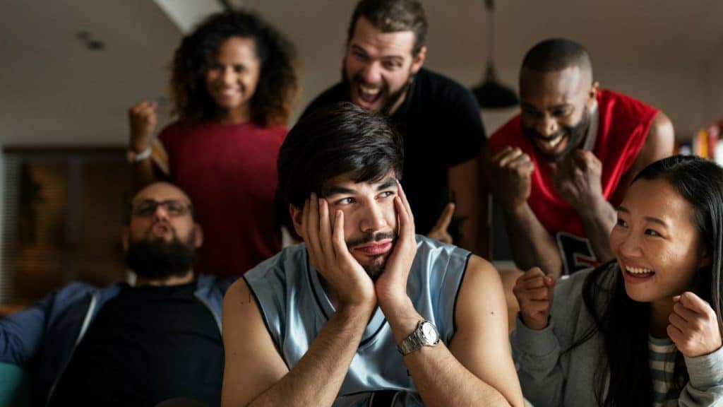 A man rests his face in his hands while people cheer and gesture behind him.