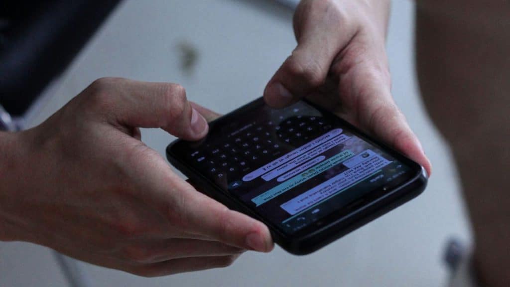 Two hands hold a black smartphone while typing a message in a messaging app.