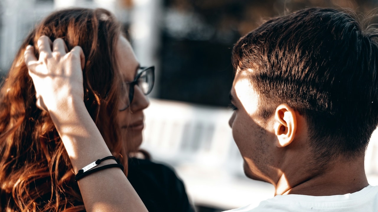 Man in a white shirt and woman wearing black sunglasses are sitting together outdoors.