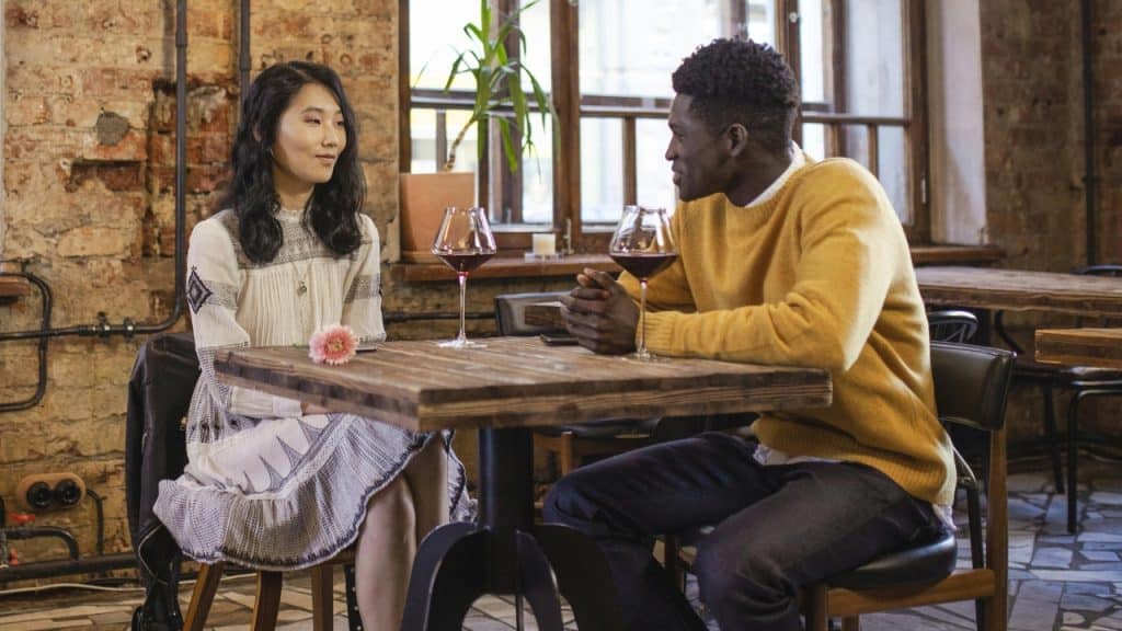 A woman in a white dress and a man in a yellow sweater sit at a table.