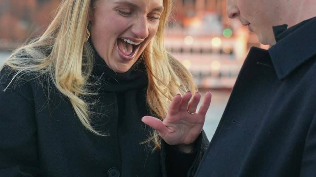A woman reacting with surprise while looking at her hand as a man stands beside her.
