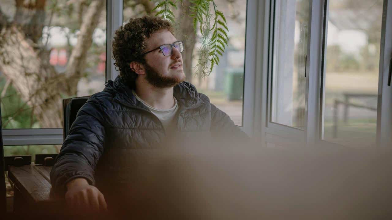 A man wearing glasses sits by a window