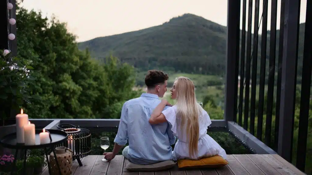 A couple sitting on a deck, looking at each other with a mountain view.