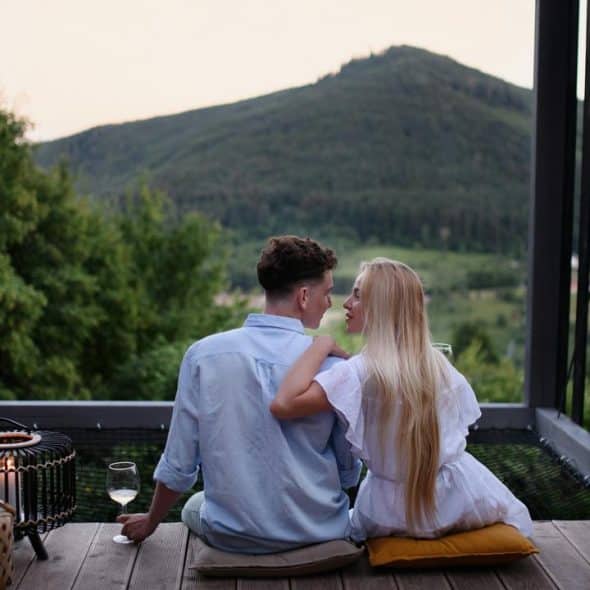 A couple sitting on a deck, looking at each other with a mountain view.