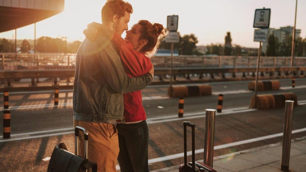 A couple hugging warmly with suitcases at an airport during sunset