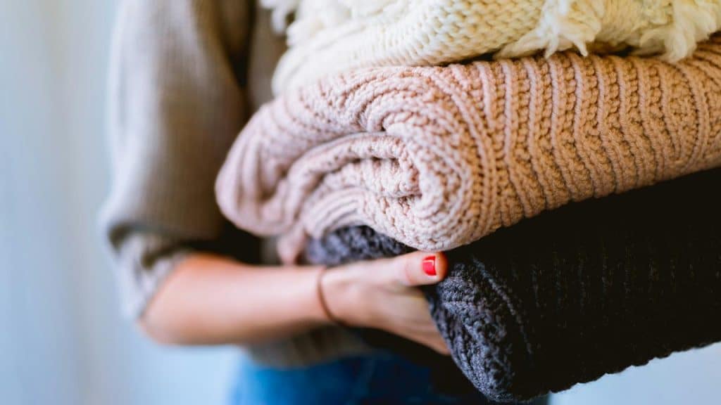 A person holds a stack of folded knit sweaters.