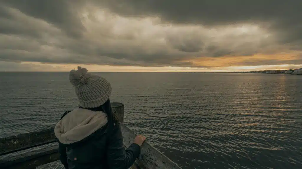 A person standing on a pier and looking out over the water at sunset.