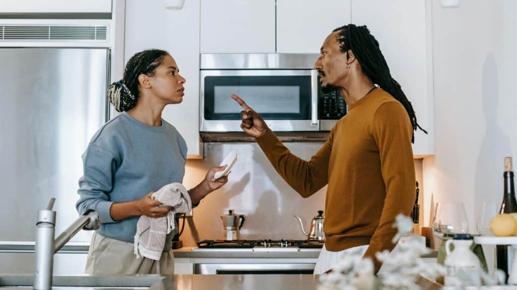 A man points a finger at a woman holding a dish towel in a kitchen.