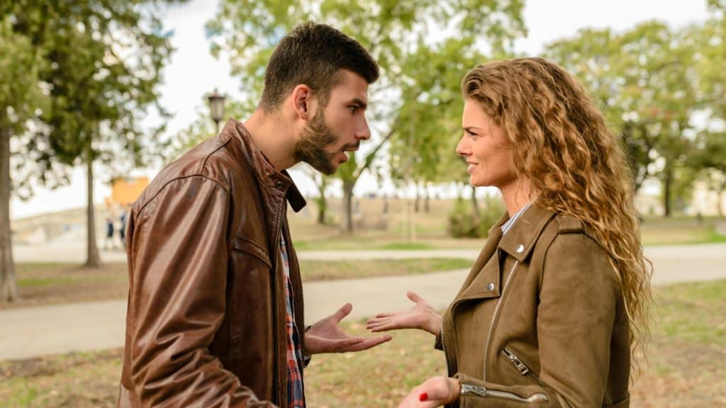 A man and woman in leather jackets facing each other and gesturing in a park.