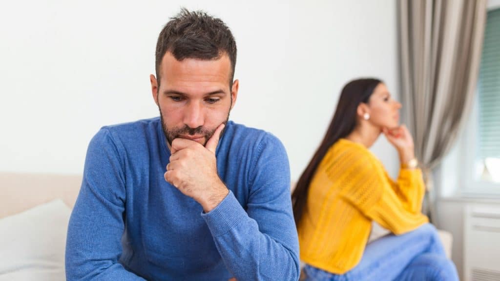 A man in a blue sweater sits with his chin on his hand near a woman.