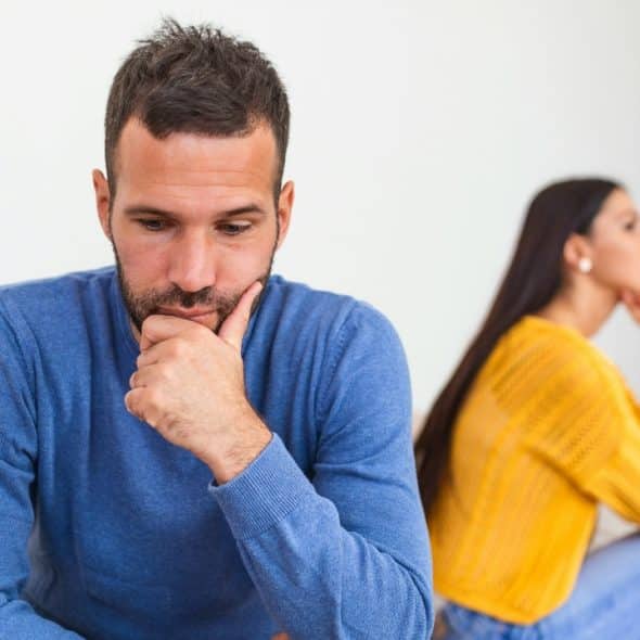 A man in a blue sweater sits with his chin on his hand near a woman.