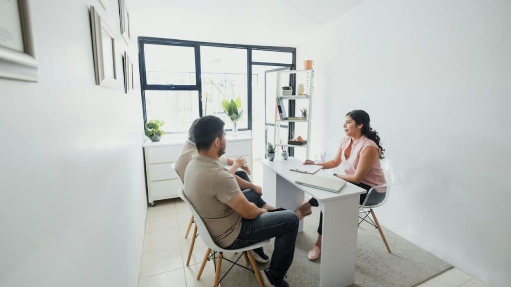 A young woman psychologist with a couple patients in therapy talking about mental problems while the doctor is listening and making notes.