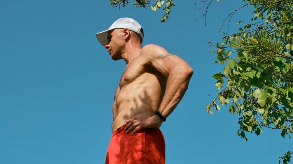 A shirtless man in red shorts and a white cap looks out under a blue sky.