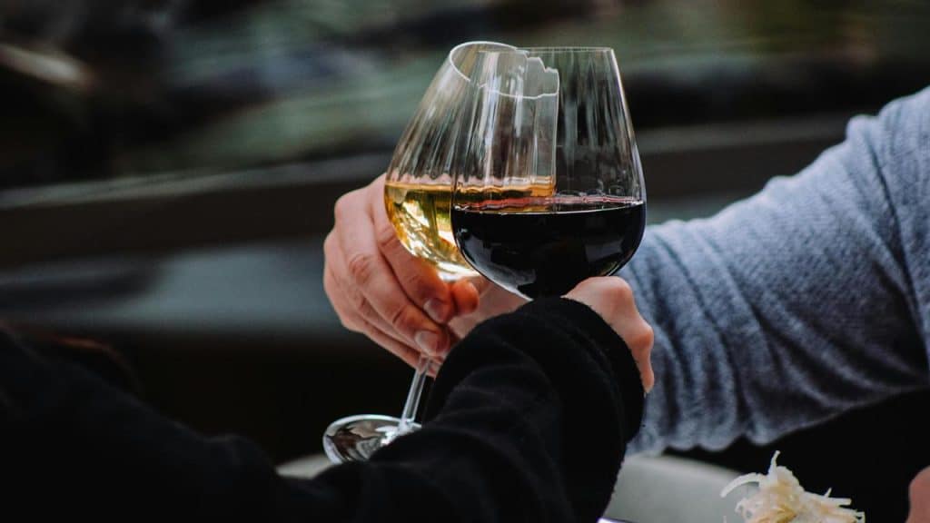 A close-up of two people clinking glasses of red and white wine.