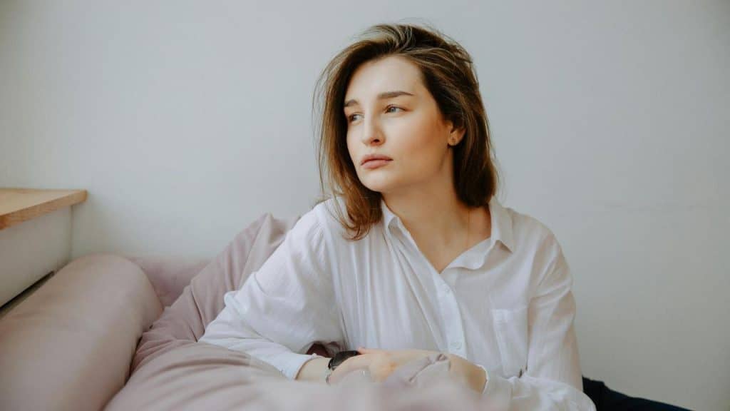 A woman in a white shirt sitting on a couch and looking thoughtfully to the side.