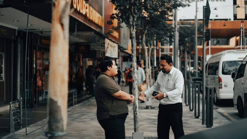 A man in a white dress shirt and black pants is standing on a sidewalk during daytime.