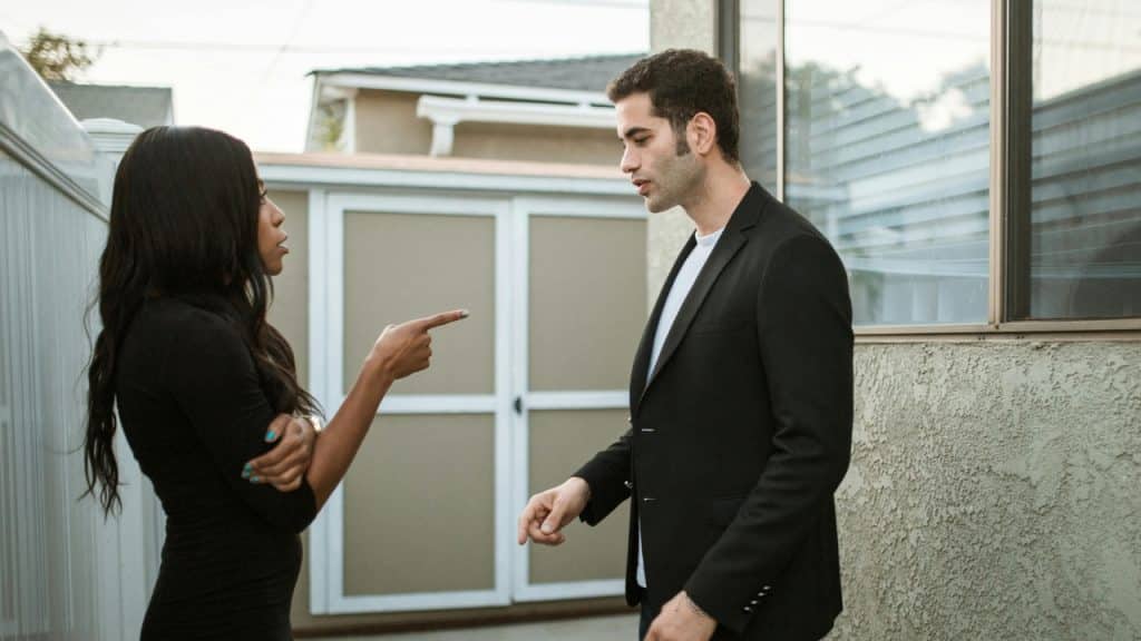 A woman points her finger at a man while they have a serious conversation outside.