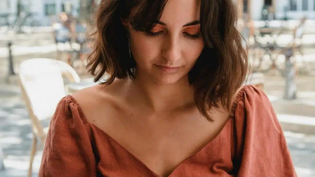 A woman in a rust-colored top looking down while sitting at an outdoor café table.