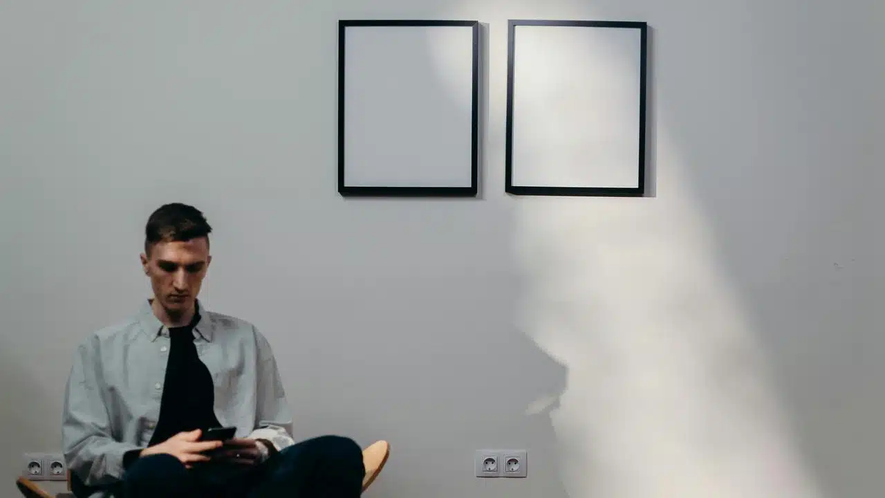 A man sitting in a minimalist room using a smartphone