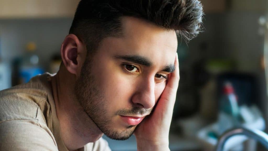 A pensive man resting his face on his hand indoors.