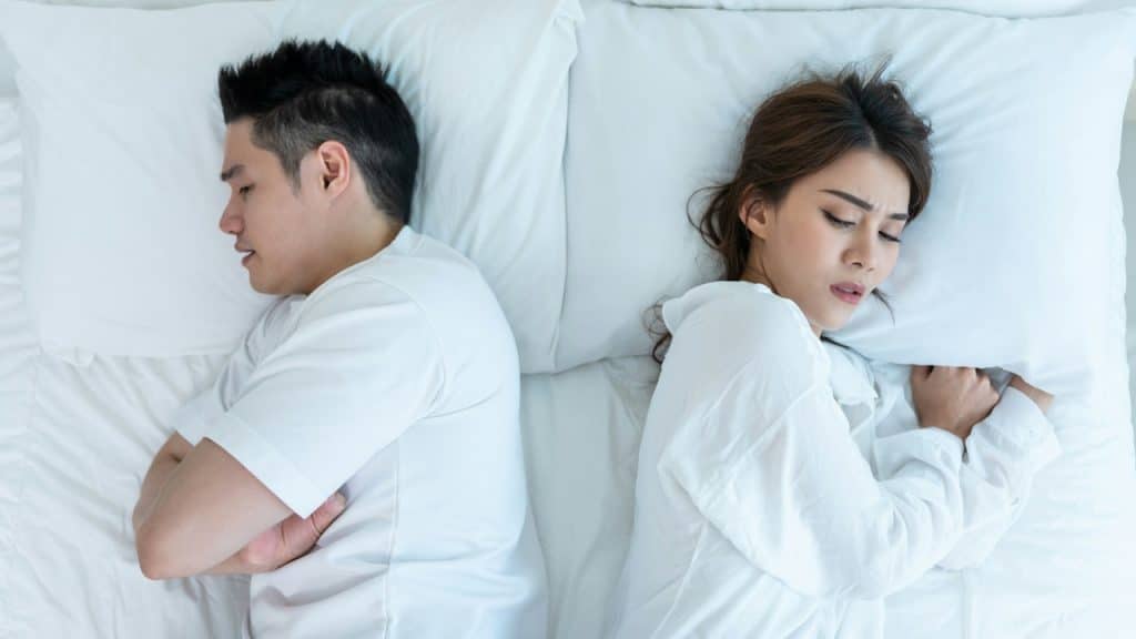 An upset man and a woman lying on a bed after a big fight.