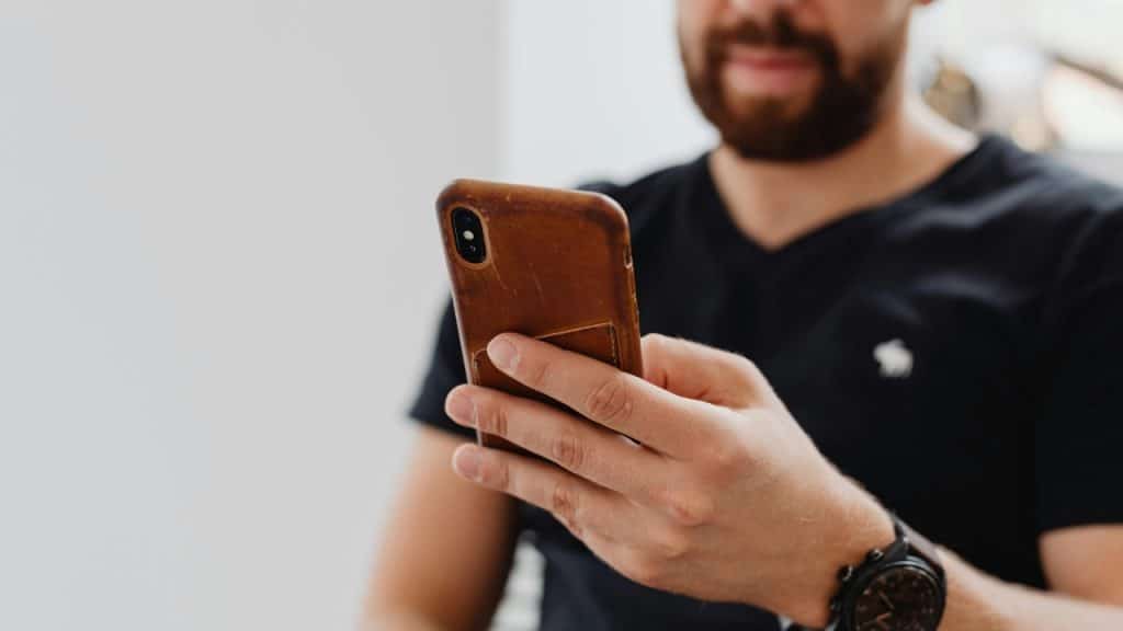 A man with a beard holds a smartphone with a leather case in his hand.