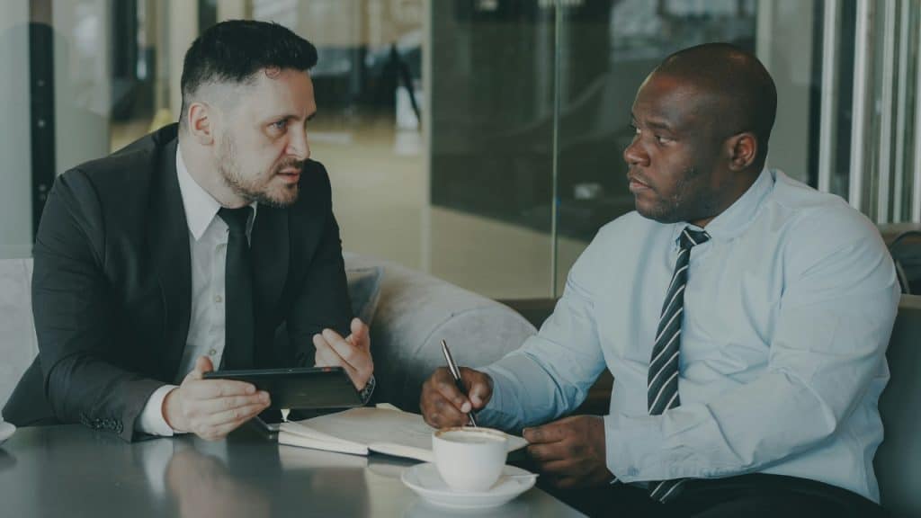 Two men in suits sit at a table while having a serious business discussion.