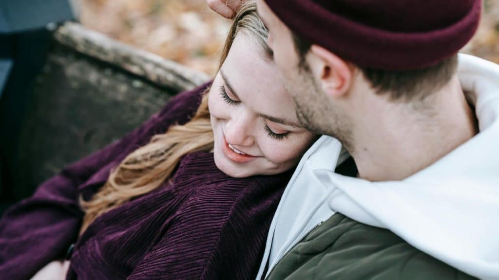 A couple cuddling together outdoors on a bench.