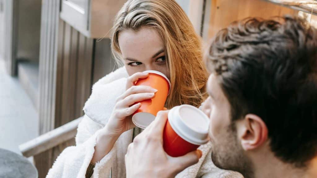 A couple drinking coffee together and smiling at each other.