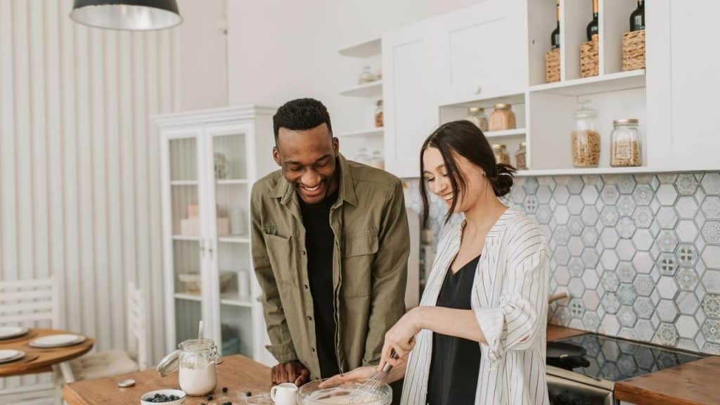 A couple smiling and cooking together in a cozy kitchen.