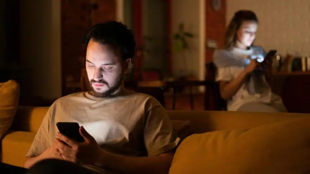 A man and woman sitting apart using their phones at night.