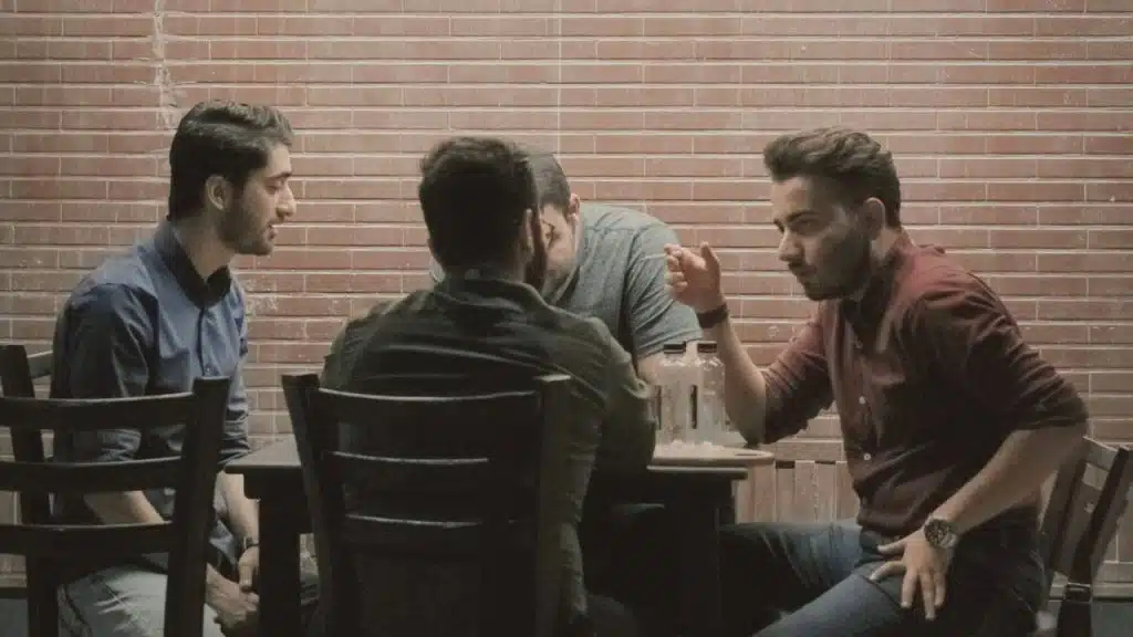 Four men sit around a table in a room with brick walls.