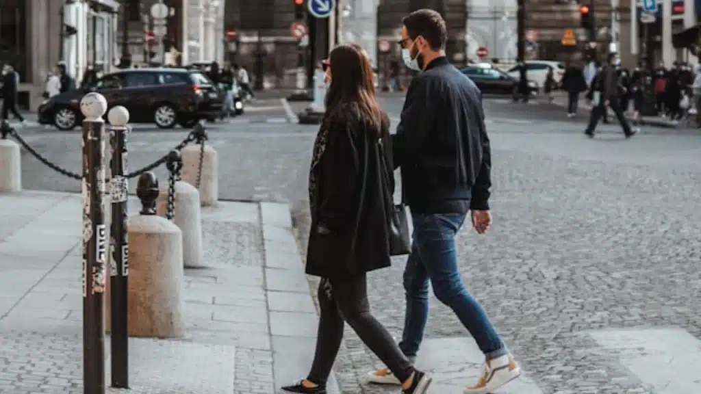 A man wearing a face mask walks beside a woman on a cobblestone city street.