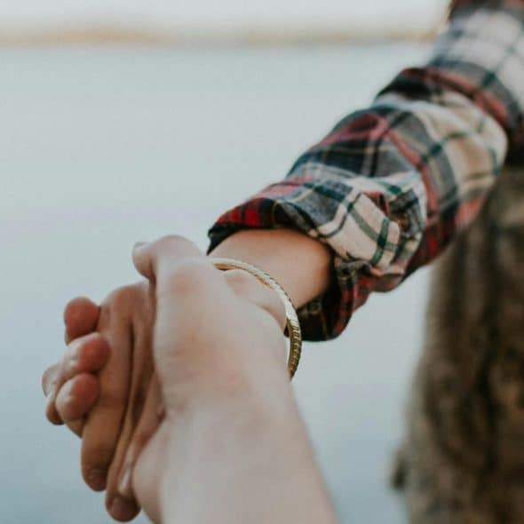 A person in a plaid shirt holding another person’s hand.