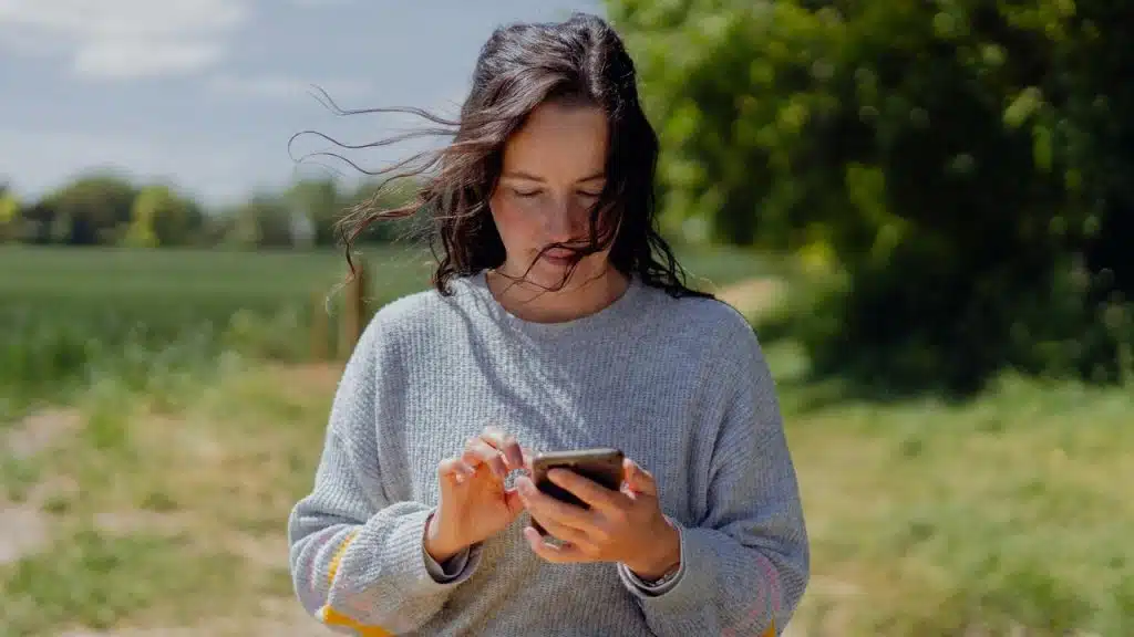 A woman standing outdoors using a smartphone.