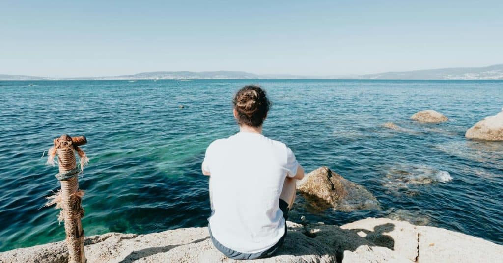 A person sitting on a rocky shore, looking out over the ocean.
