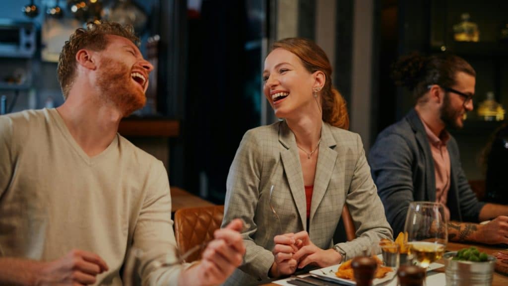 A man and woman laugh while sitting together at a table during a meal.